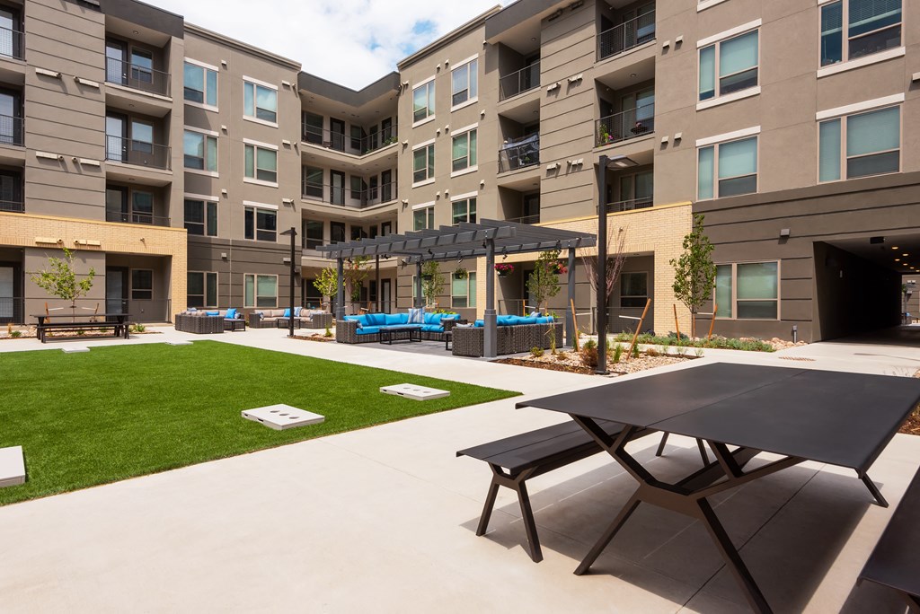 a patio with a picnic table and lounge chairs in front of an apartment building  at Encore at Boulevard One, Denver