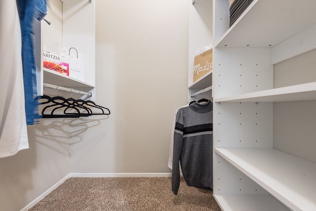 a walk in closet with white shelving and a coat rack