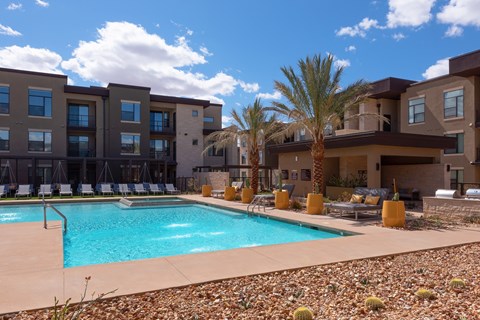 A swimming pool is surrounded by chairs and palm trees in front of a building.