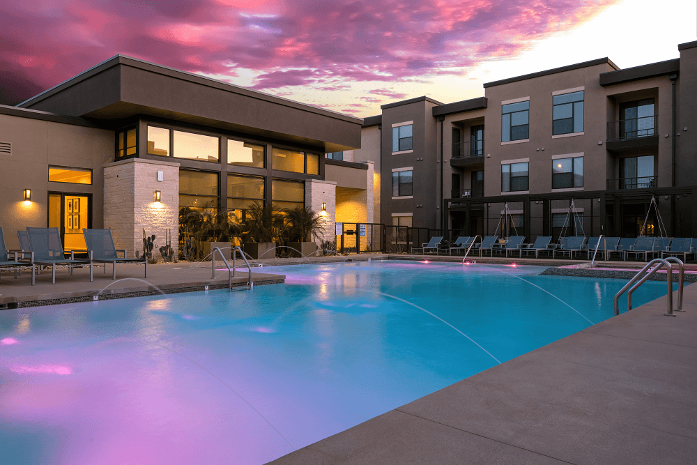 a swimming pool in front of an apartment building at sunset