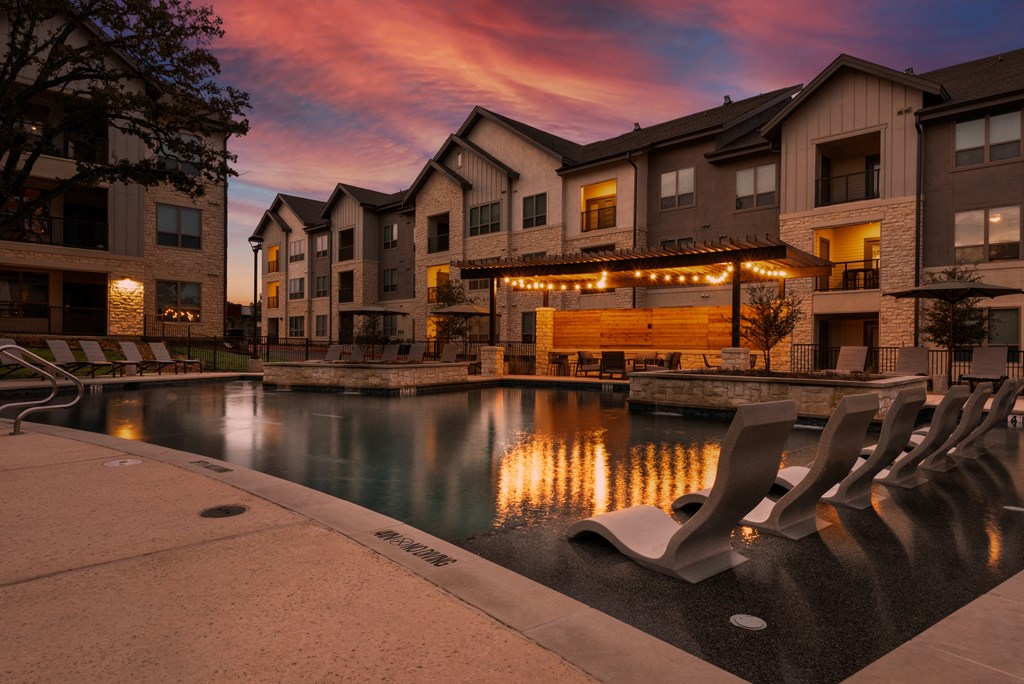 an empty swimming pool at night with apartments in the background