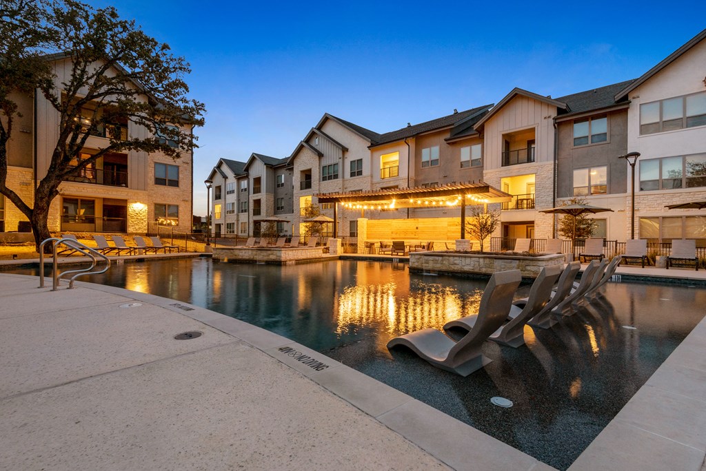 a swimming pool at night with apartments in the background