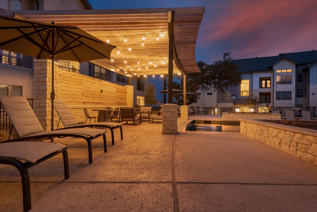 a patio with chairs and umbrellas and a pool at night