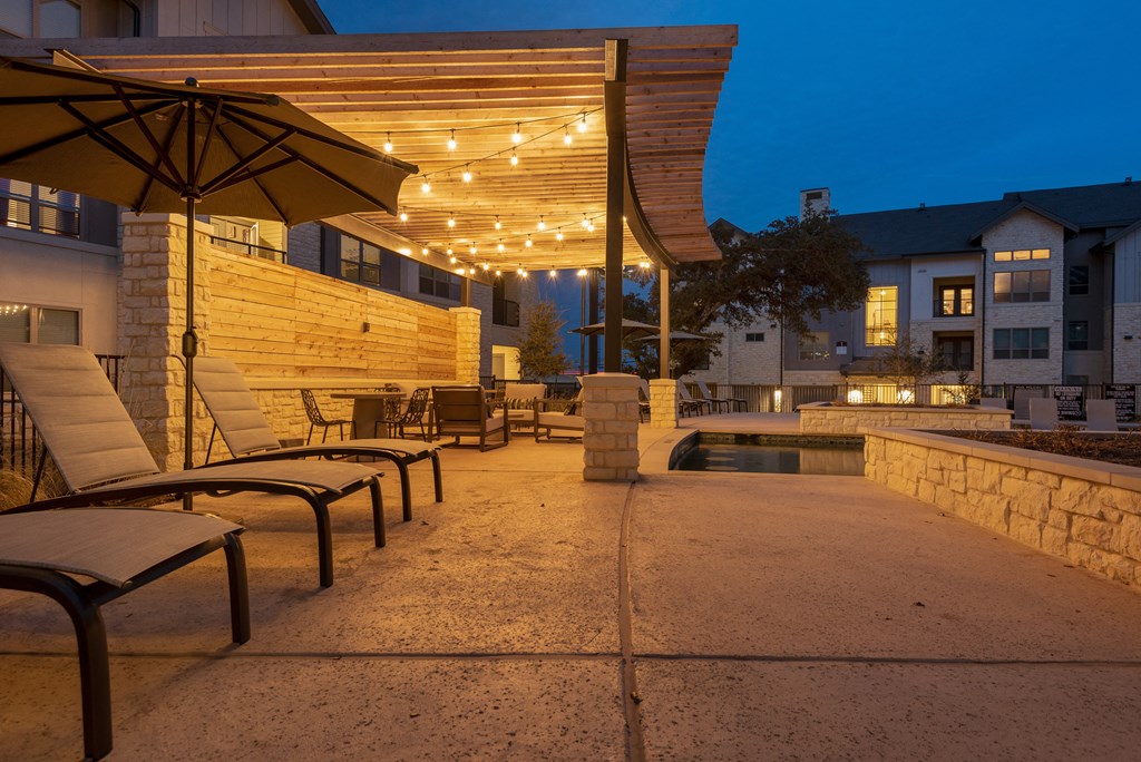 a patio with chairs and umbrellas and a pool at night