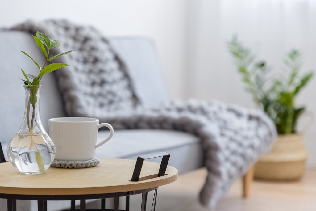 A clear glass vase with a plant sits on a table next to a white mug.