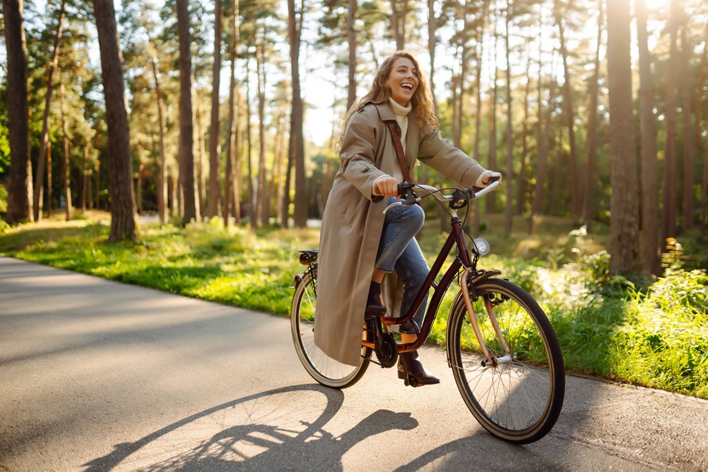 A woman is riding a bicycle on a paved path in a wooded area.