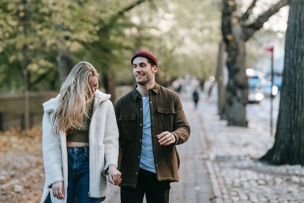 A couple walking hand in hand down a tree-lined street.