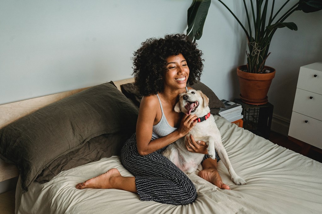 A woman with curly hair is sitting on a bed with a dog.