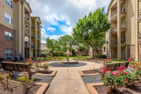 an outdoor courtyard with a fountain and benches in front of an apartment building