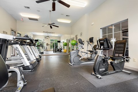 a gym with cardio machines and a ceiling fan