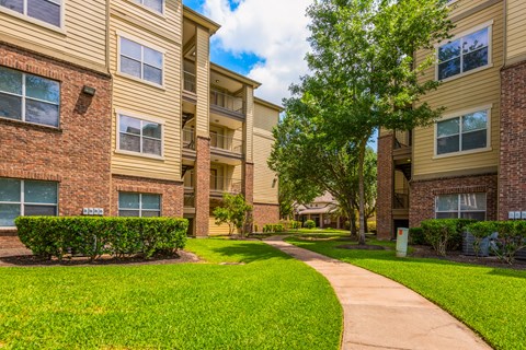 a sidewalk leading to an apartment building with green grass and trees
