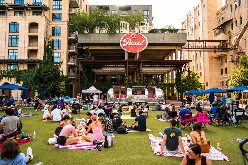 A large group of people are sitting on the grass in front of a building with a sign that reads "Pearl".