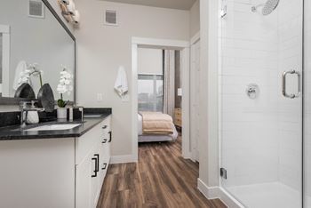 a bathroom with a large shower and a bedroom in the background