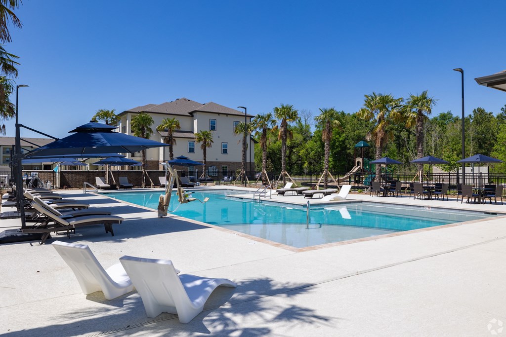 resort style swimming pool surrounded by lounge chairs and umbrellas at Beau Chene Lake Charles Apartments in Lake Charles, LA 70605