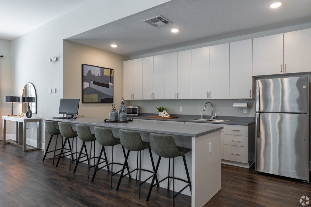 a clubhouse kitchen with a large island with bar stools and a stainless steel refrigerator at Beau Chene Lake Charles Apartments in Lake Charles, LA 70605