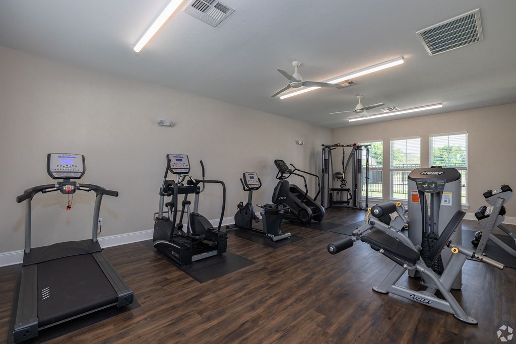 a gym with cardio machines and other exercise equipment on a wooden floor at Beau Chene Lake Charles Apartments in Lake Charles, LA 70605