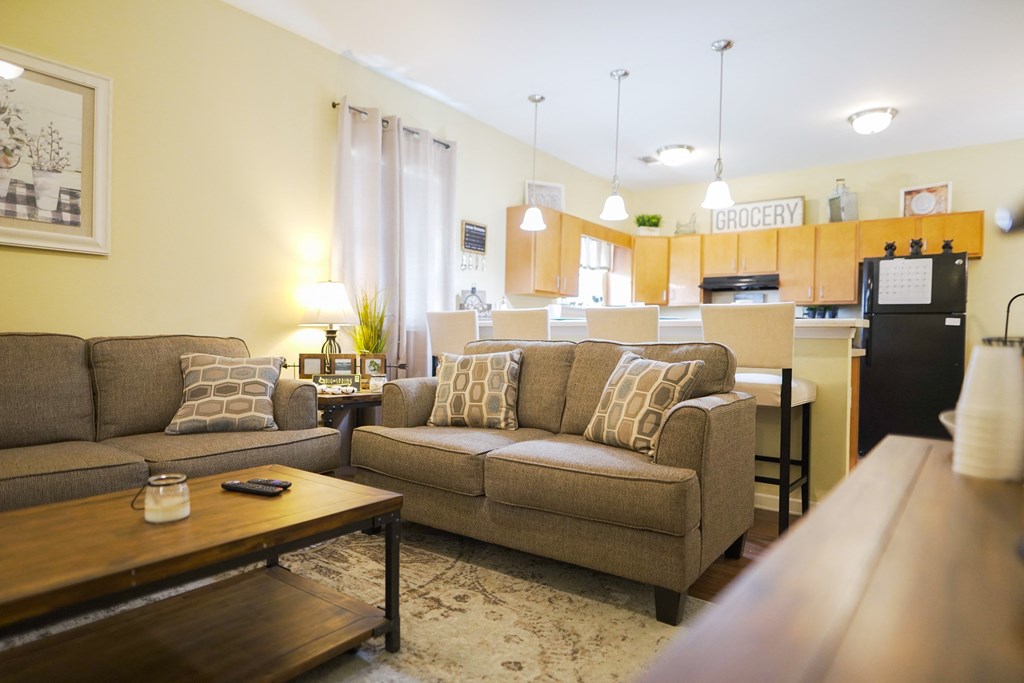A living room with a couch, a coffee table, and a kitchen area in the background.