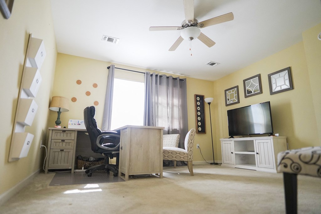 A room with a ceiling fan and a desk with a chair.