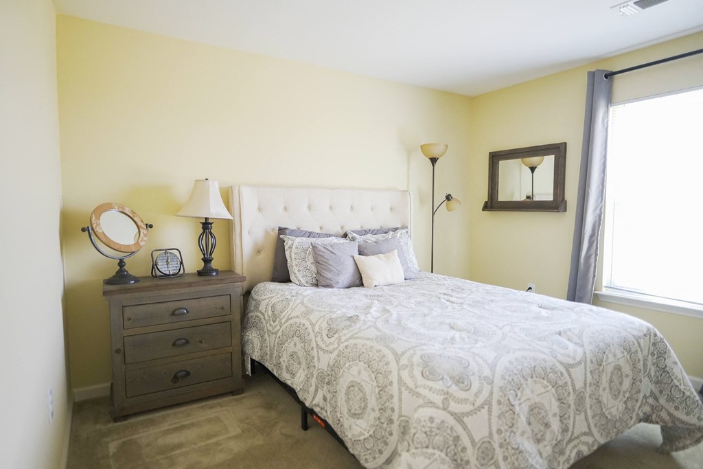 A bedroom with a queen bed, nightstand, and lamp.