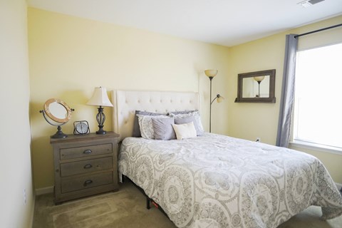 A bedroom with a queen bed, nightstand, and lamp.