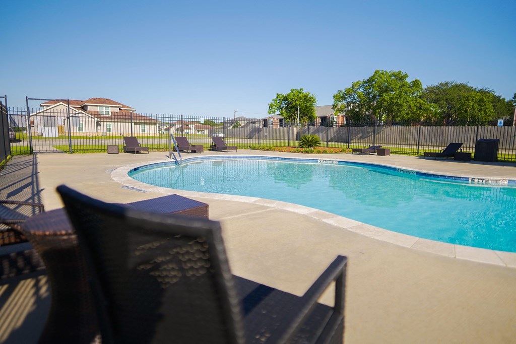 a swimming pool with chairs around it in front of a fence