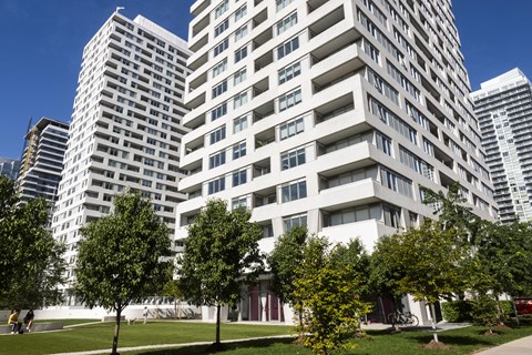 A large white building with balconies is surrounded by trees.