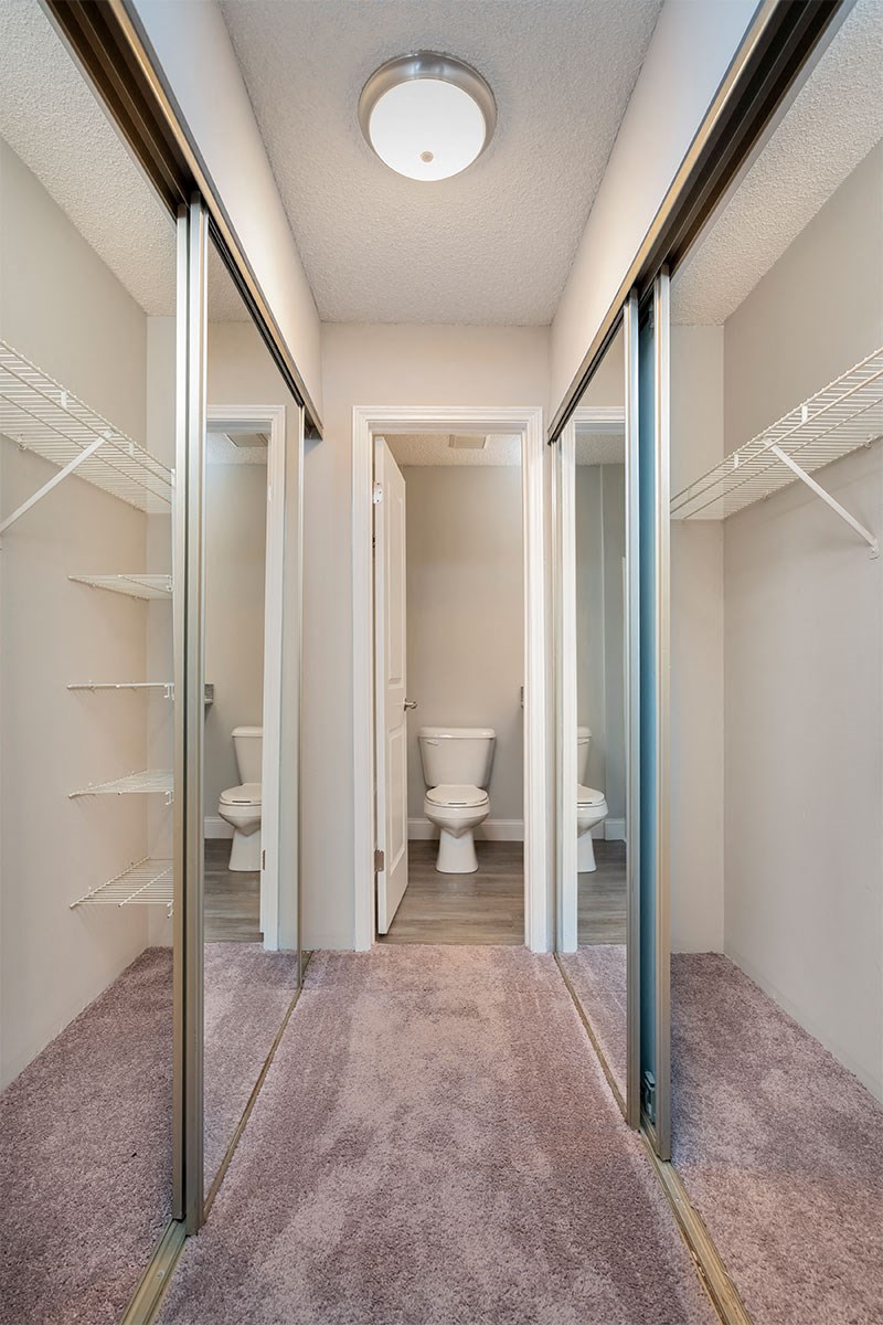 a walk in closet with a toilet and mirrored doors