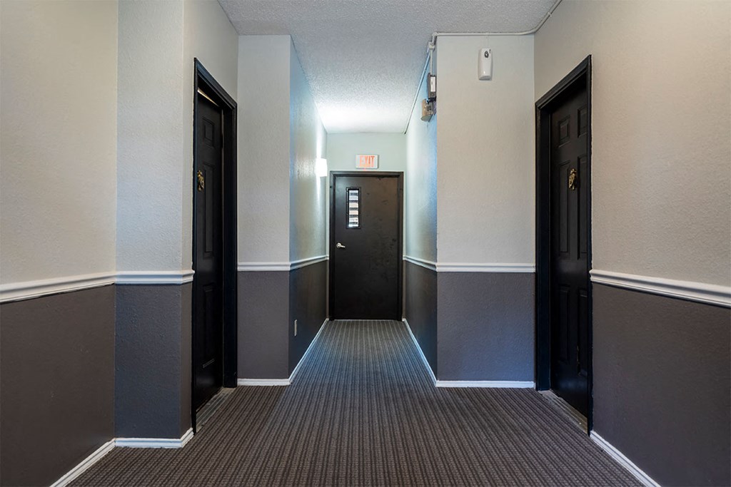 a hallway with three doors and a exit sign