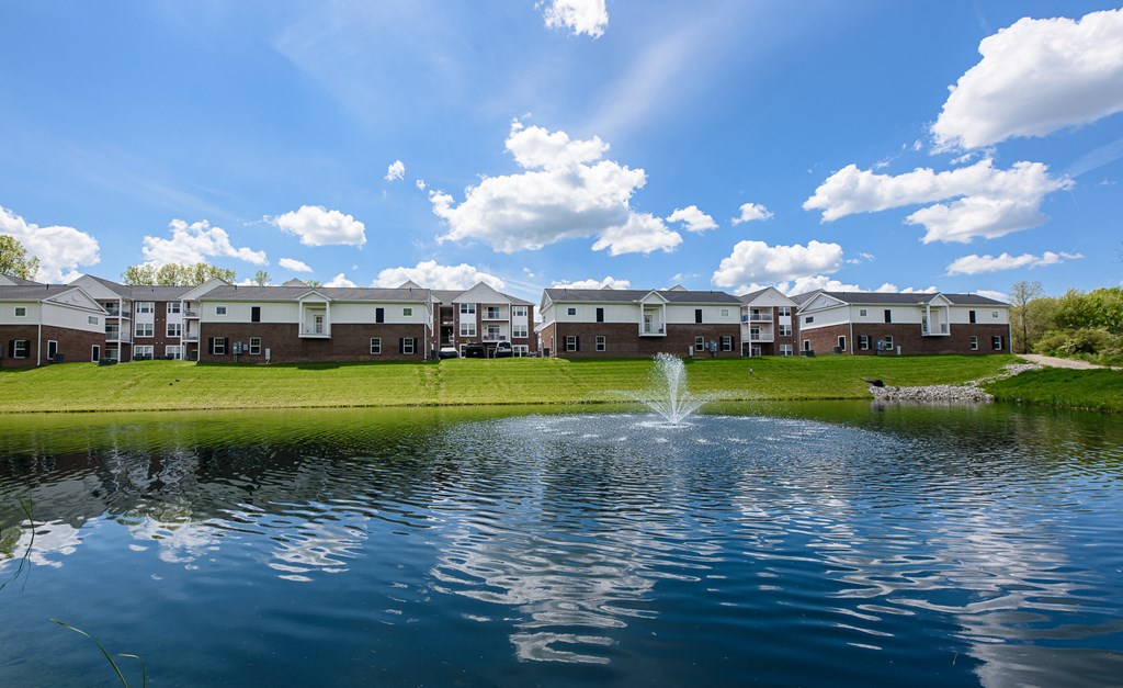 a fountain in the middle of a pond with houses in the background