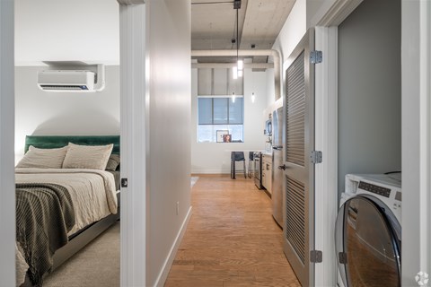 A bedroom with a bed and a washing machine in the laundry room.