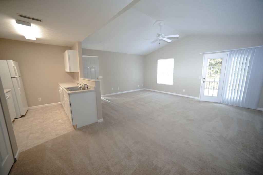 an empty living room and kitchen with a refrigerator and a sink