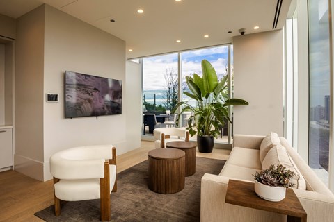 A living room with a large window, a white sofa, a white chair, a wooden coffee table, and a painting on the wall.