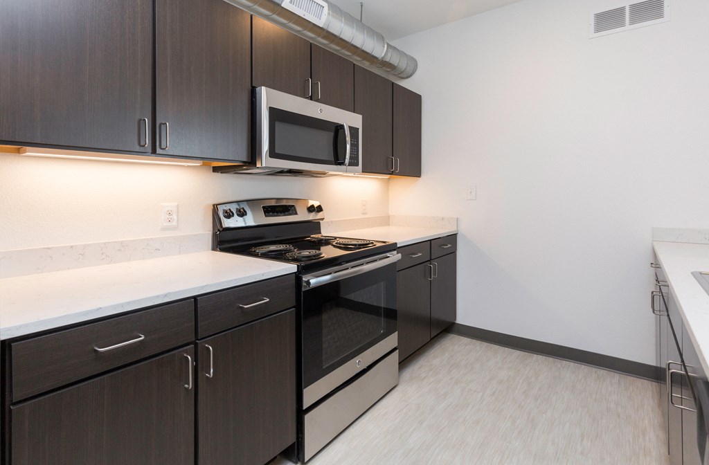 a kitchen with dark cabinets and a stove and a microwave
