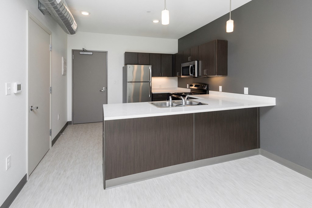 an empty kitchen with a white counter top and a stainless steel refrigerator