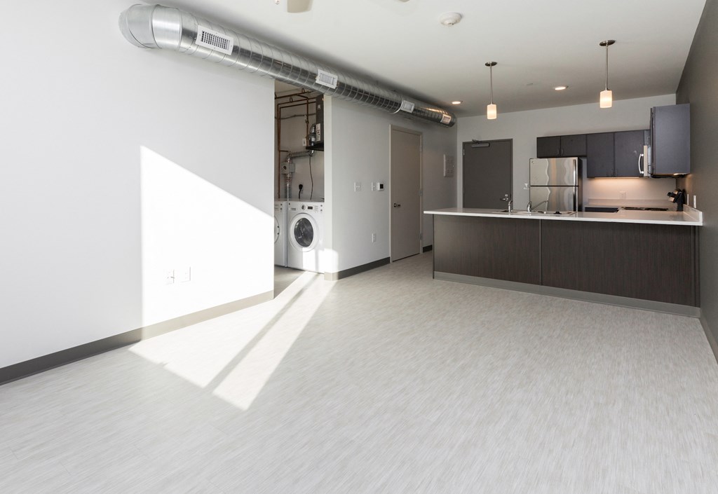 an empty living room with a kitchen and a washing machine
