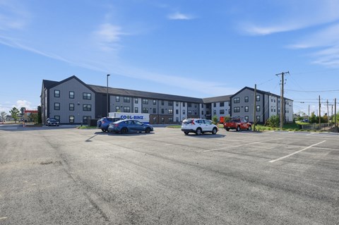 A parking lot in front of a grey building with cars parked.