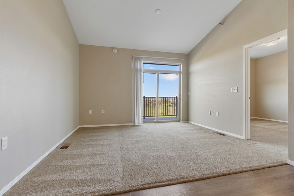 A spacious room with a carpeted floor and a view of a fence through a glass door.