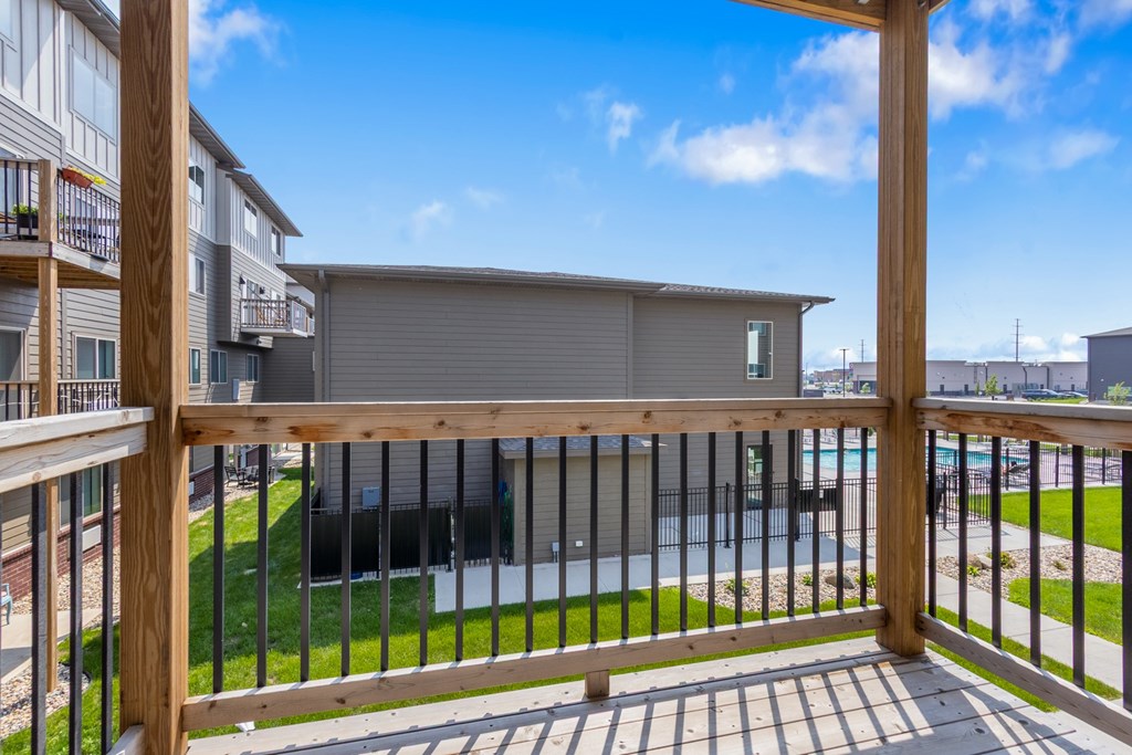 A balcony with a wooden railing overlooks a grassy area and a building.