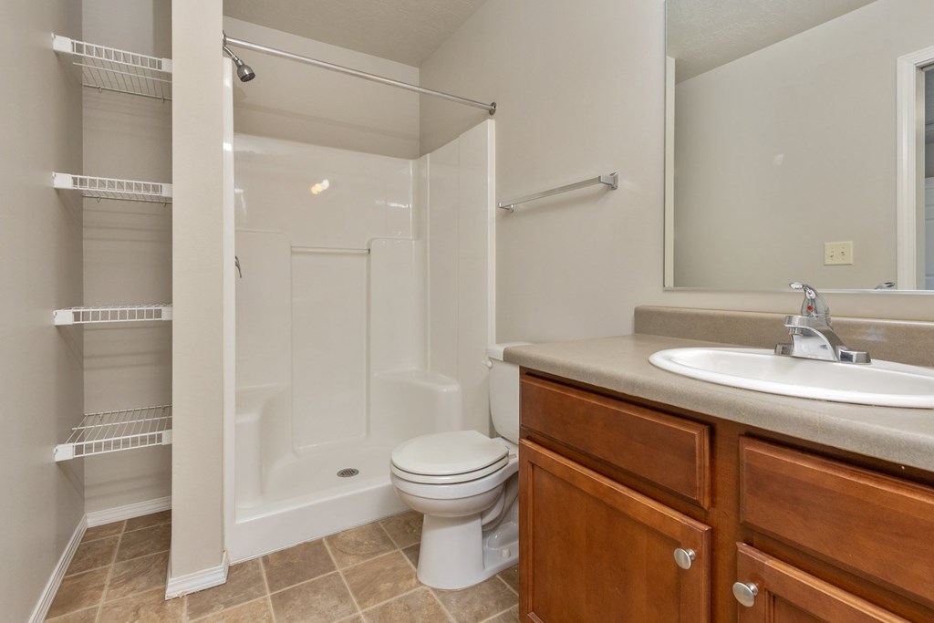 A white toilet sits in a bathroom next to a sink and a walk-in shower.