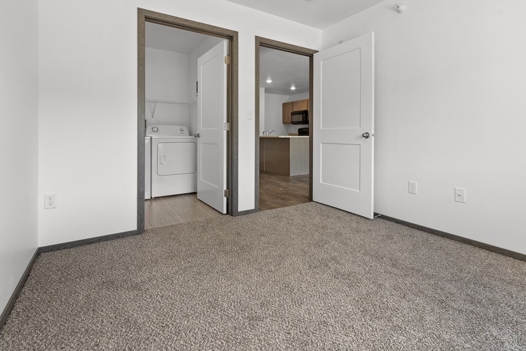 A carpeted room with a white door and a brown door.
