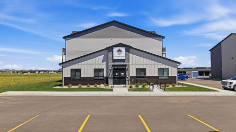 A large grey building with a black door and windows is surrounded by a parking lot.