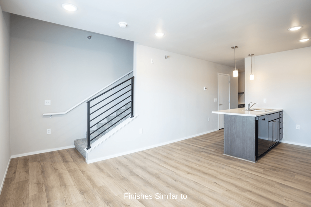 a renovated living room and kitchen with white walls and wood floors