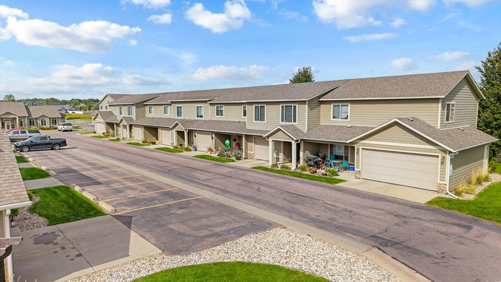 A residential street with houses on both sides and cars parked on the side.