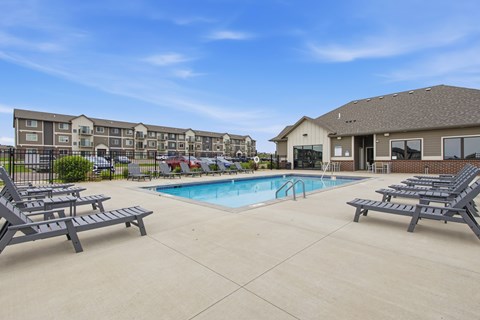 A swimming pool surrounded by lounge chairs in front of apartment buildings.