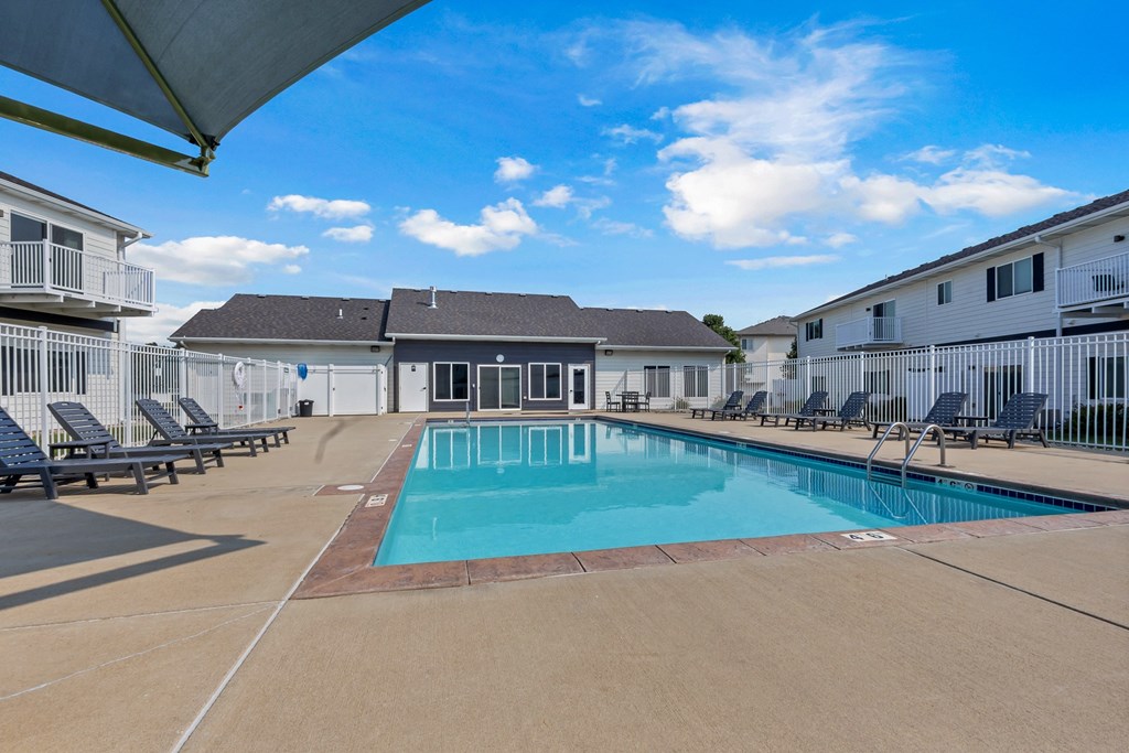 A swimming pool surrounded by sun loungers and apartment buildings.