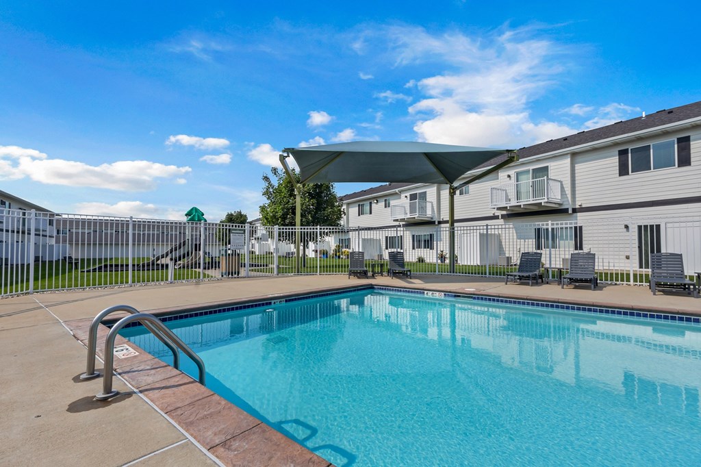 A swimming pool in front of a building with a white fence and trees.