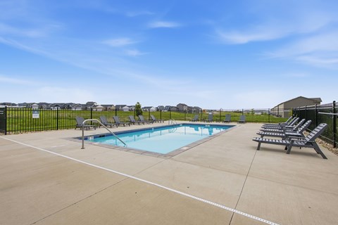 A pool surrounded by a black fence with sun loungers on the side.