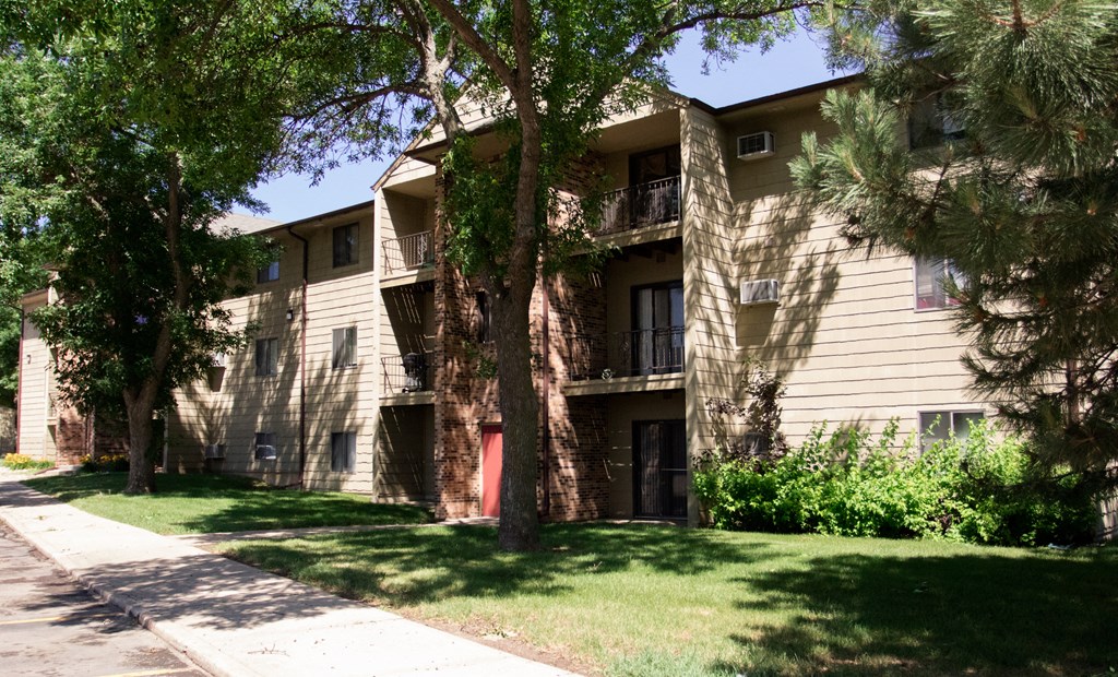 an apartment building with a lawn and trees in front of it