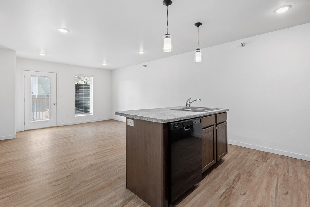 an empty living room with a kitchen with a sink and a counter top
