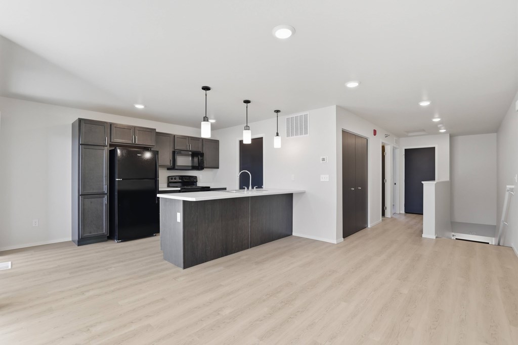 A kitchen with a black fridge and microwave, a white counter, and a black cabinet.
